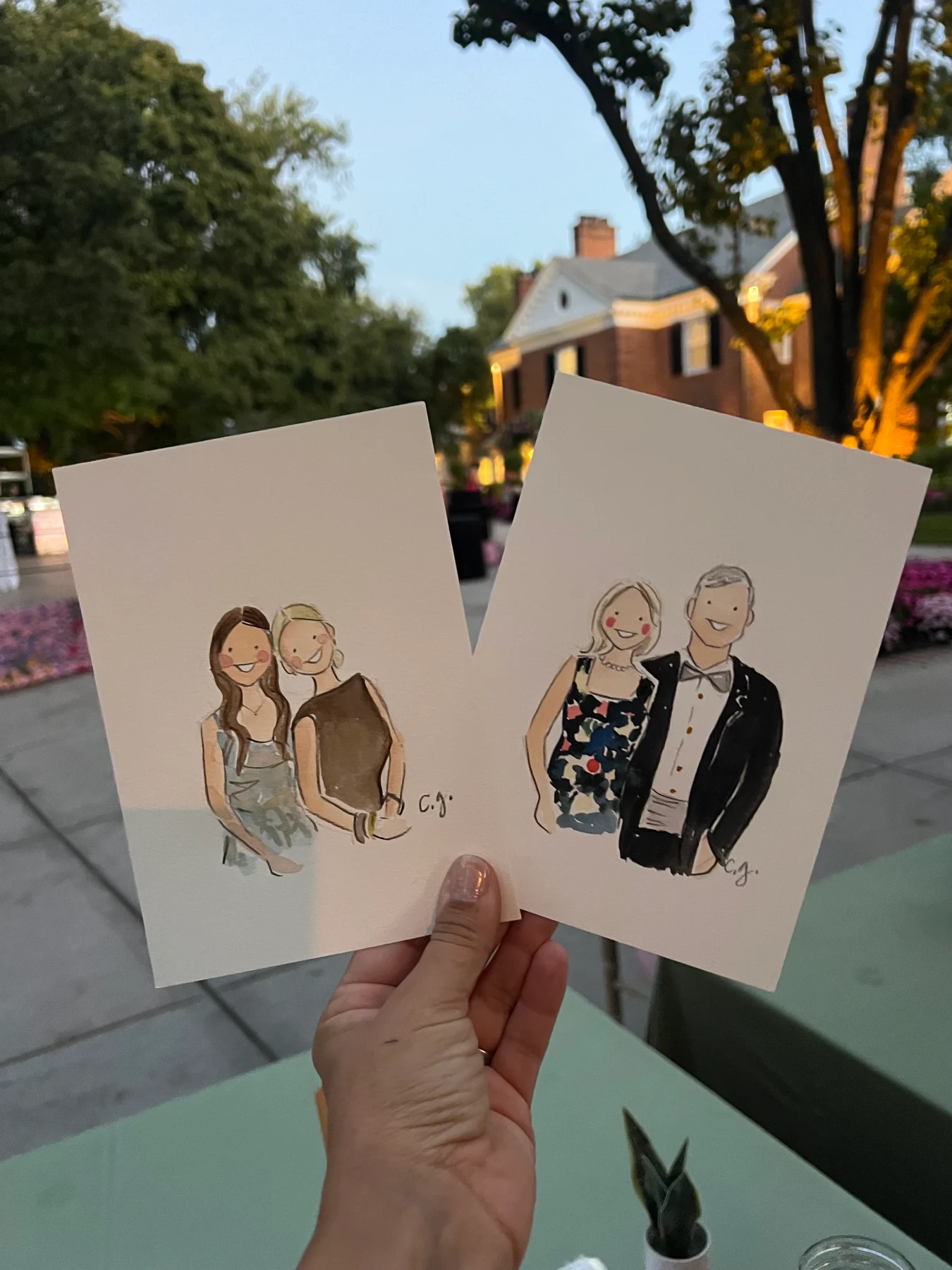 Two watercolor guest portraits held up at an evening celebration