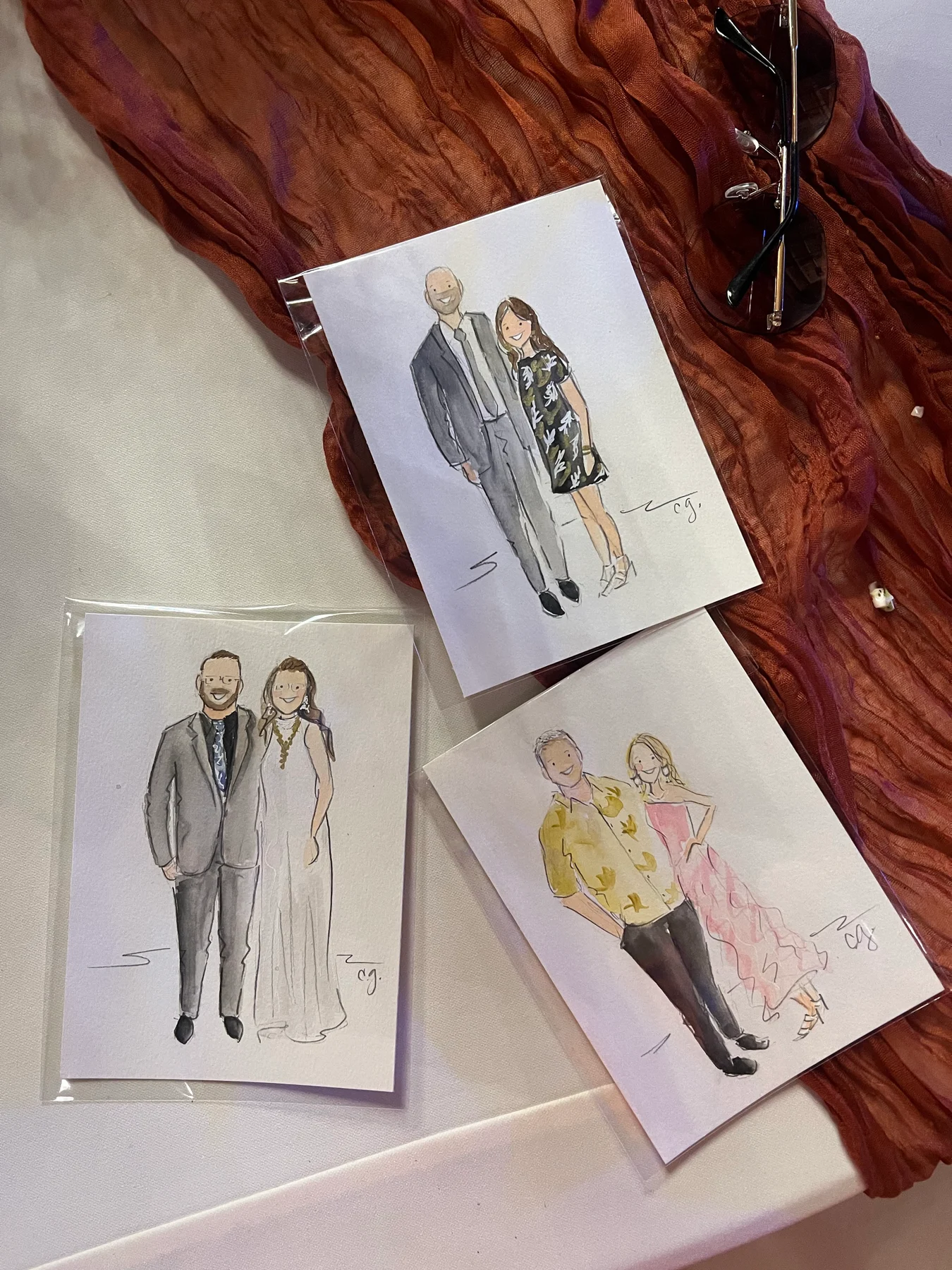 Three full-length watercolor couple portraits in protective sleeves