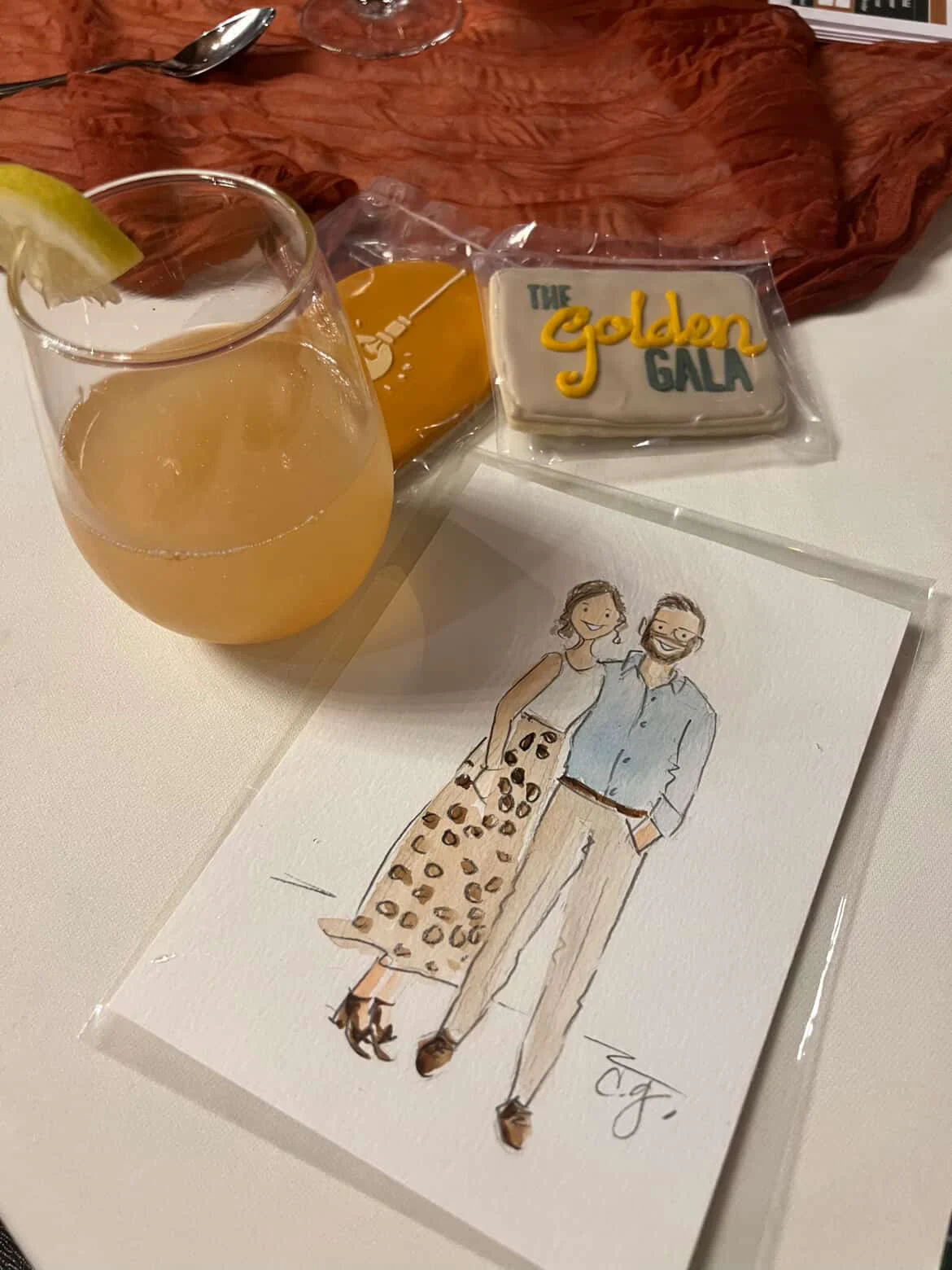 A finished watercolor guest portrait beside a drink and Golden Gala favors