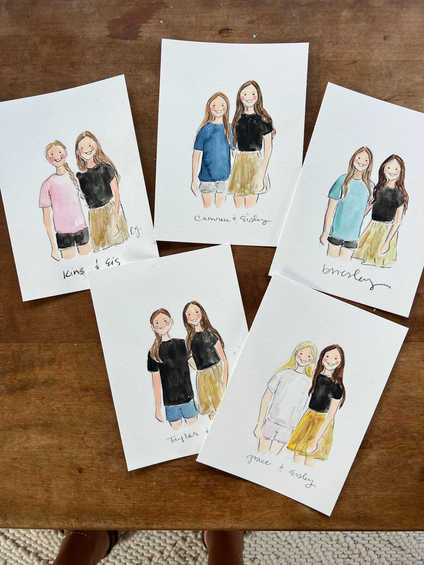 A collection of watercolor friendship portraits on a wooden table